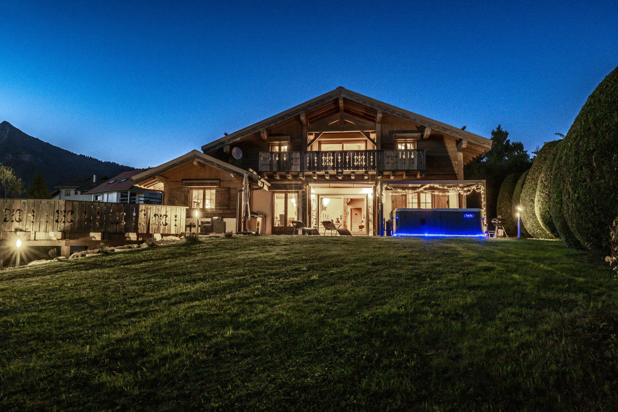 Chalet et jacuzzi vus depuis le jardin à la nuit tombée